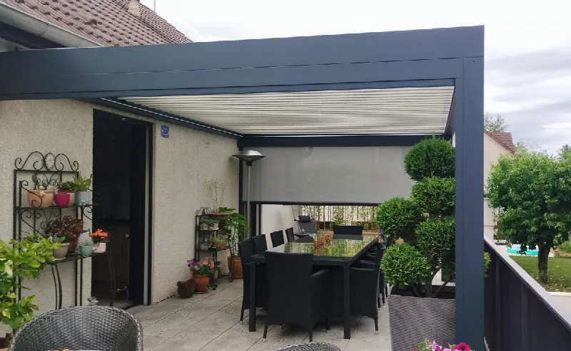 Pergola grise au-dessus d'une table de jardin, store fermé au fond