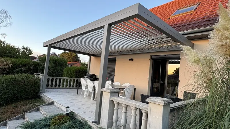 Pergola grise aux lames ouvertes sur une terrasse bordée d'une balustrade