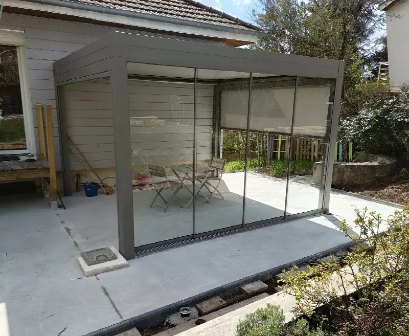 Pergola grise fermée sur les côtés par des vitrages coulissants