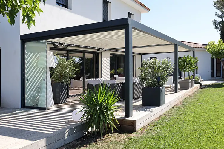 Pergola grise sur une terrasse en bois au bord d'une pelouse, panneau vitré sur le côté