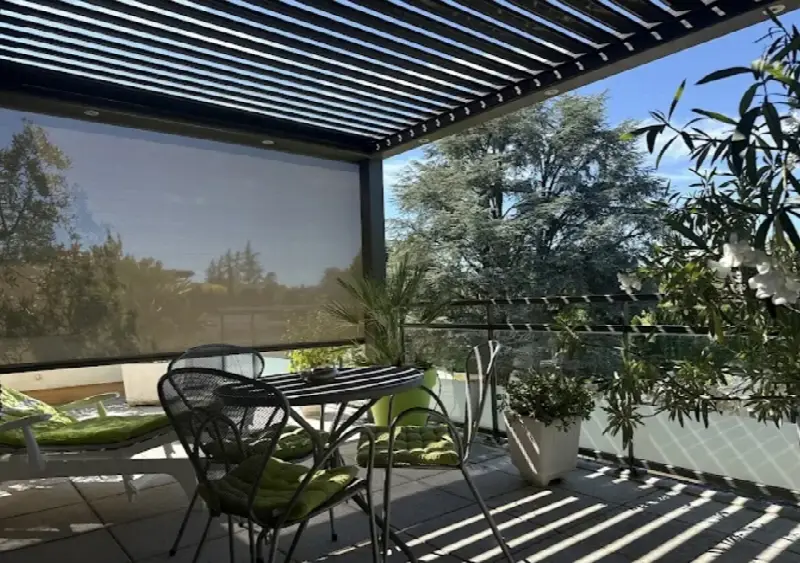 Terrasse meublée sous une pergola à lames orientables, store descendu sur un côté