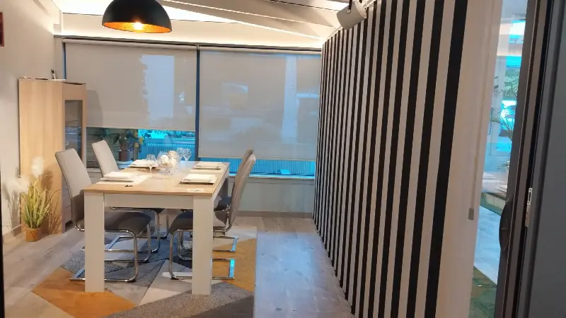 Salle à manger de véranda équipée de stores enrouleurs tamisants et de stores à bandes verticales noir et blanc