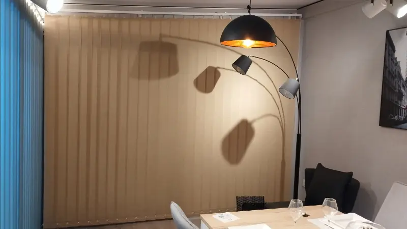 Store à bandes verticales ocre fermé, qui tamise la lumière d’un coin salon