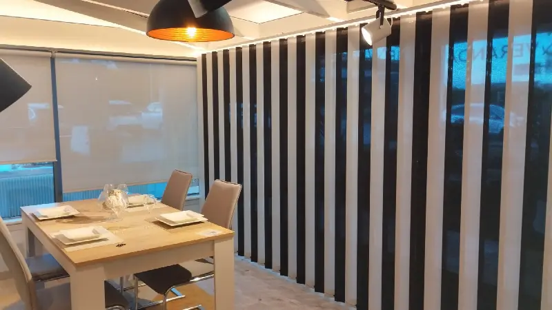 Stores verticaux noir et blanc fermés derrière une table de salle à manger, stores enrouleurs aux fenêtres