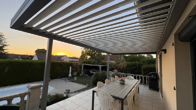Pergola à lames ouvertes au-dessus d'une grande table, au coucher du soleil